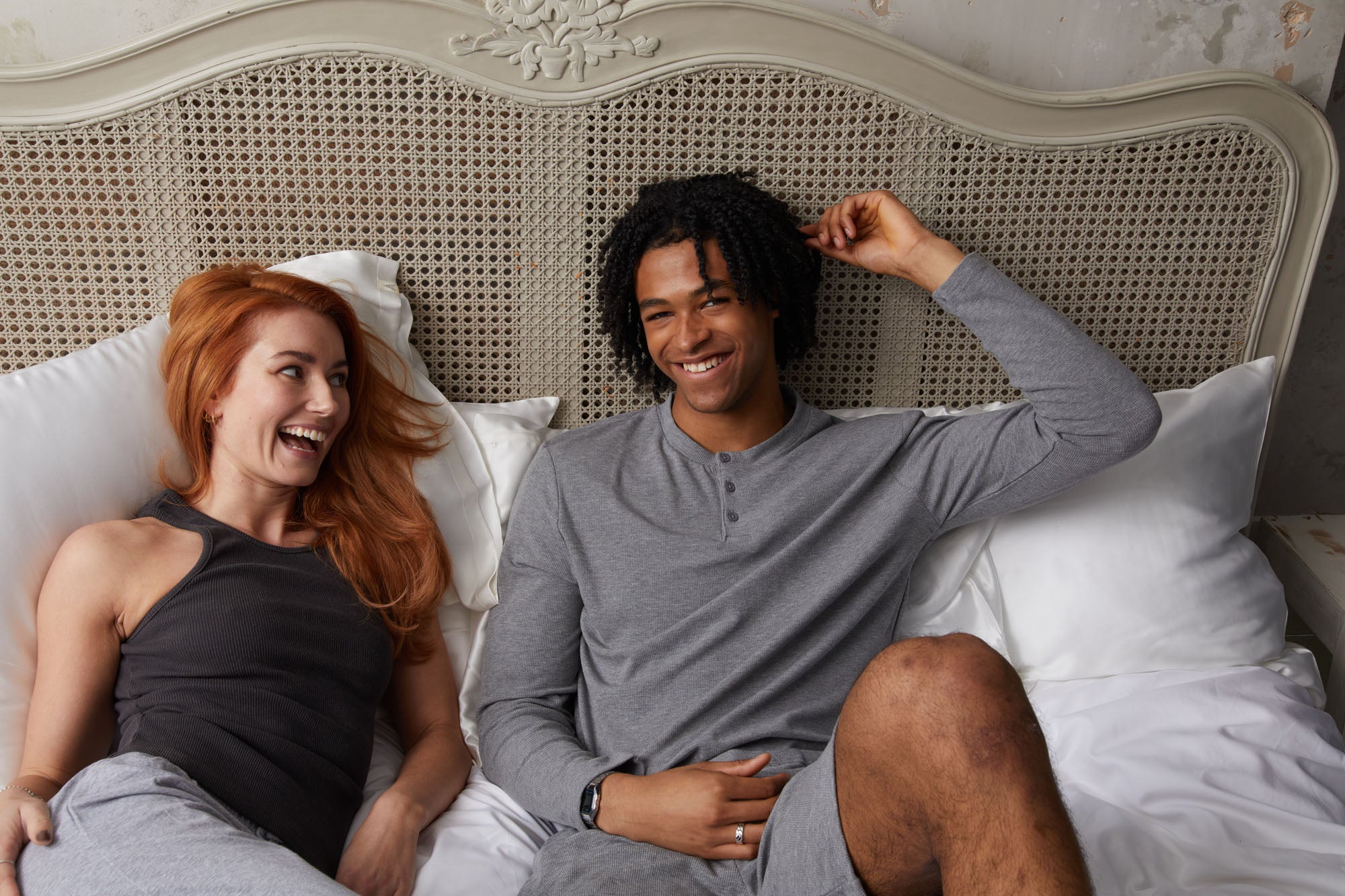 Couple laughing in bed with white silk pillowcases all around them