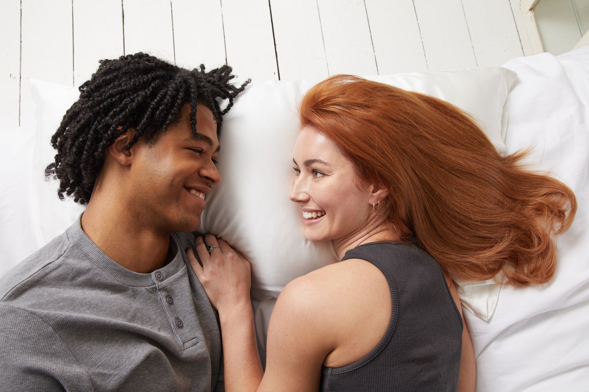 Couple lying on white ethical silk pillowcases smiling at each other