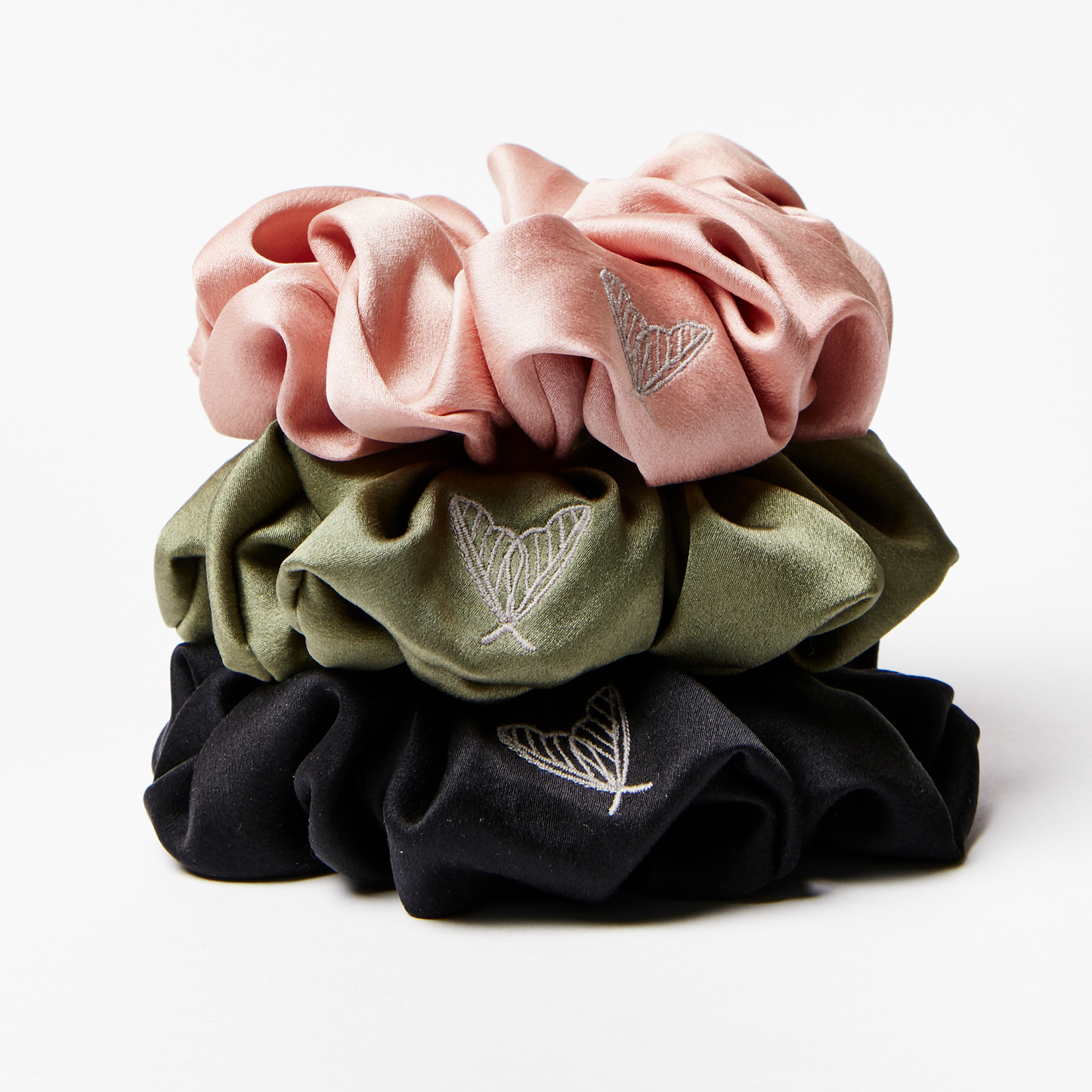 Silk scrunchies in a stack, in pink, green and black silk with ethical silk moth embroidery